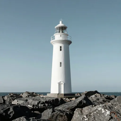 Photograph of a white lighthouse on dark rocks under a plain sky