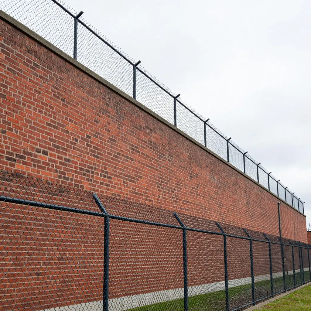A long brick wall with a chain link fence in front of it and another fence along the top
