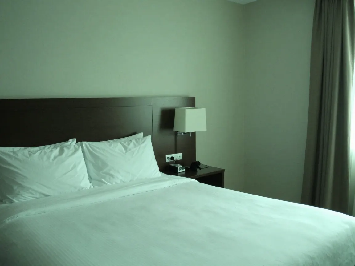 Hotel bed and bedside lamp under a flat green colour cast