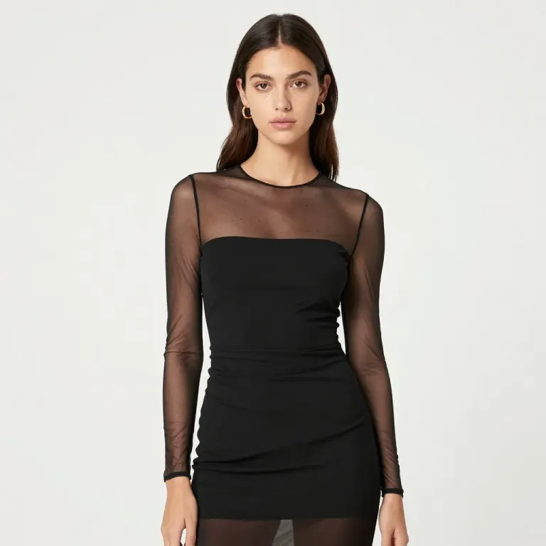 A woman in a black dress with sheer mesh sleeves against a plain pale backdrop
