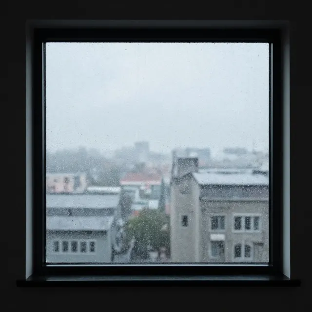 A window looking out at a grey city with a few drops on the glass