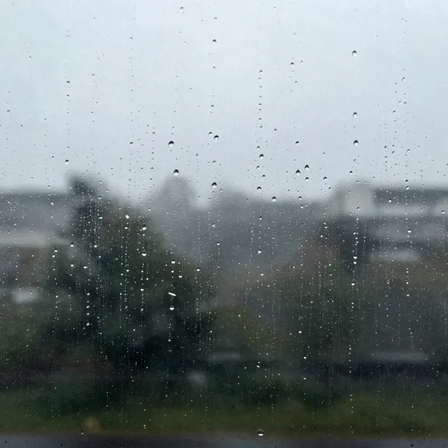 A window covered in raindrops with the city blurred behind them