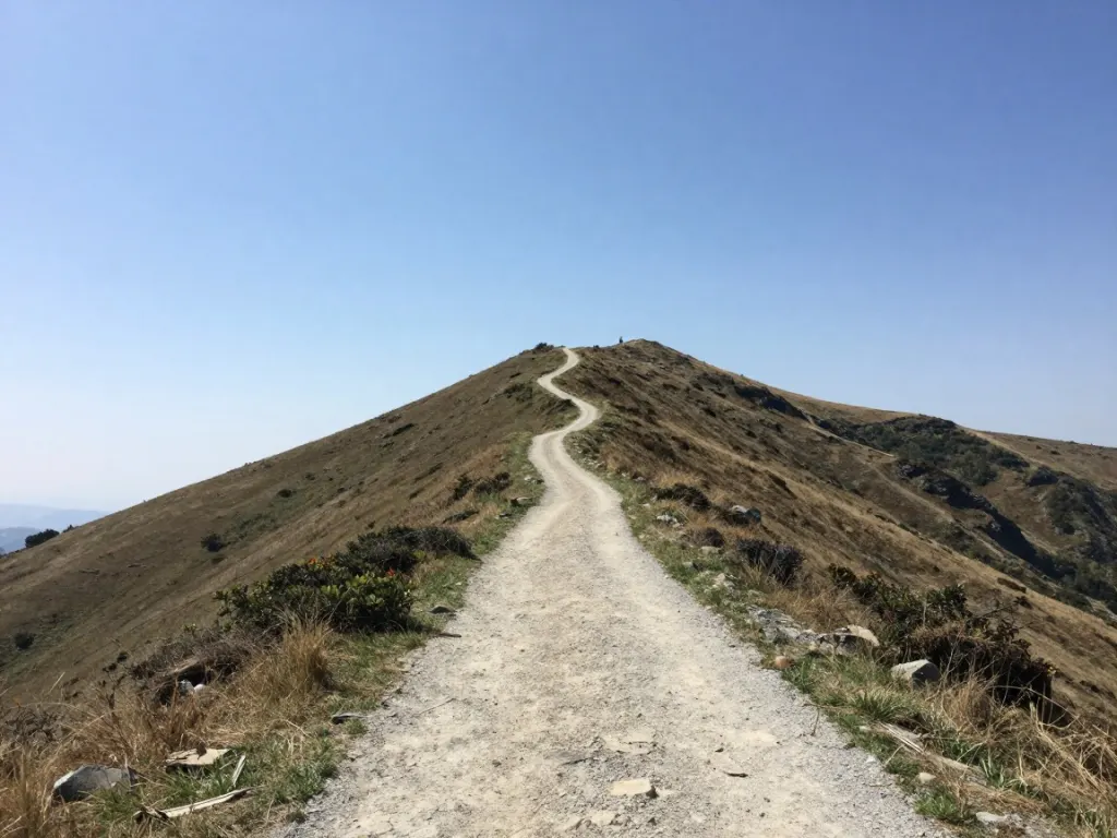 A dirt mountain path along a sunny ridge under a clear blue sky