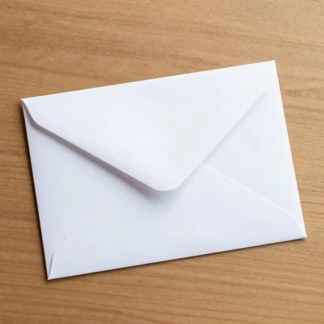 A crisp white envelope lying on a warm wooden table