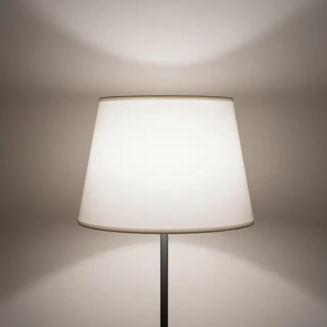 A white lampshade lit from inside against a warm beige wall